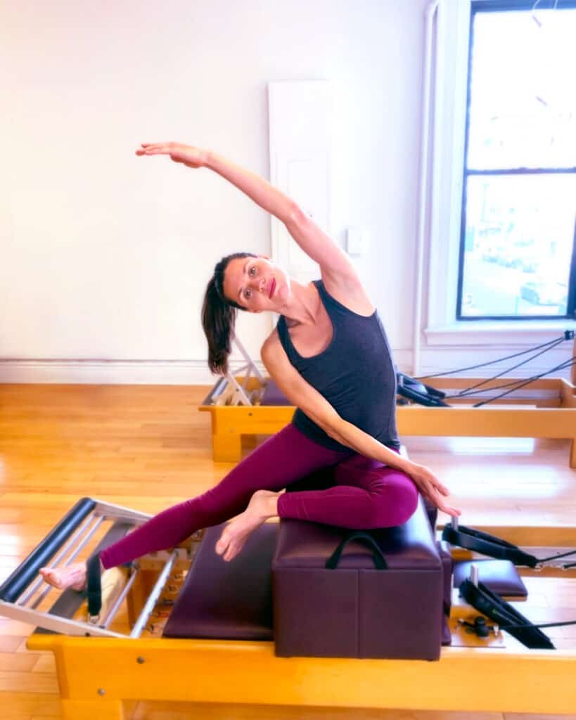 Instructor performing Mermaid on the Reformer. Pilates is the long-term game for health, success, and well-being.