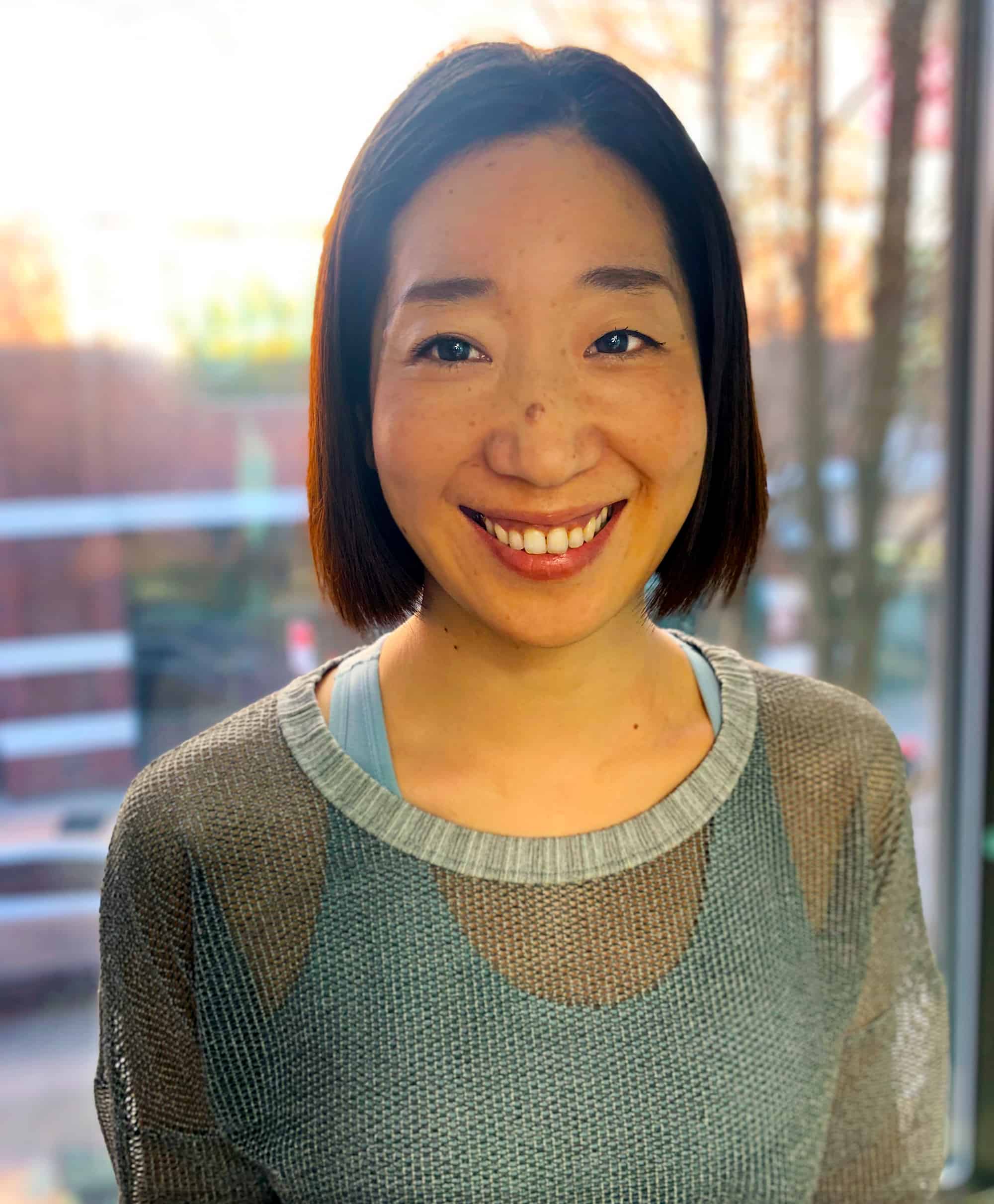 Portrait of Pilates Instructor Maho Ogawa with window and sunset behind her.